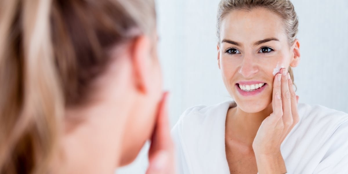 Smiling woman applying moisturizer to hydrated skin to avoid itchy skin caused by dehydration