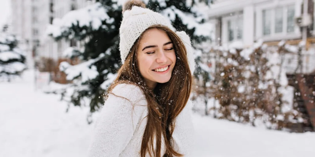 Smiling girl with long hair in the snow, showing causes of hairfall in winter.