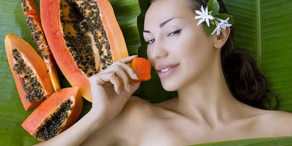 A woman holding a slice of papaya, highlighting papaya benefits for skin and hair.