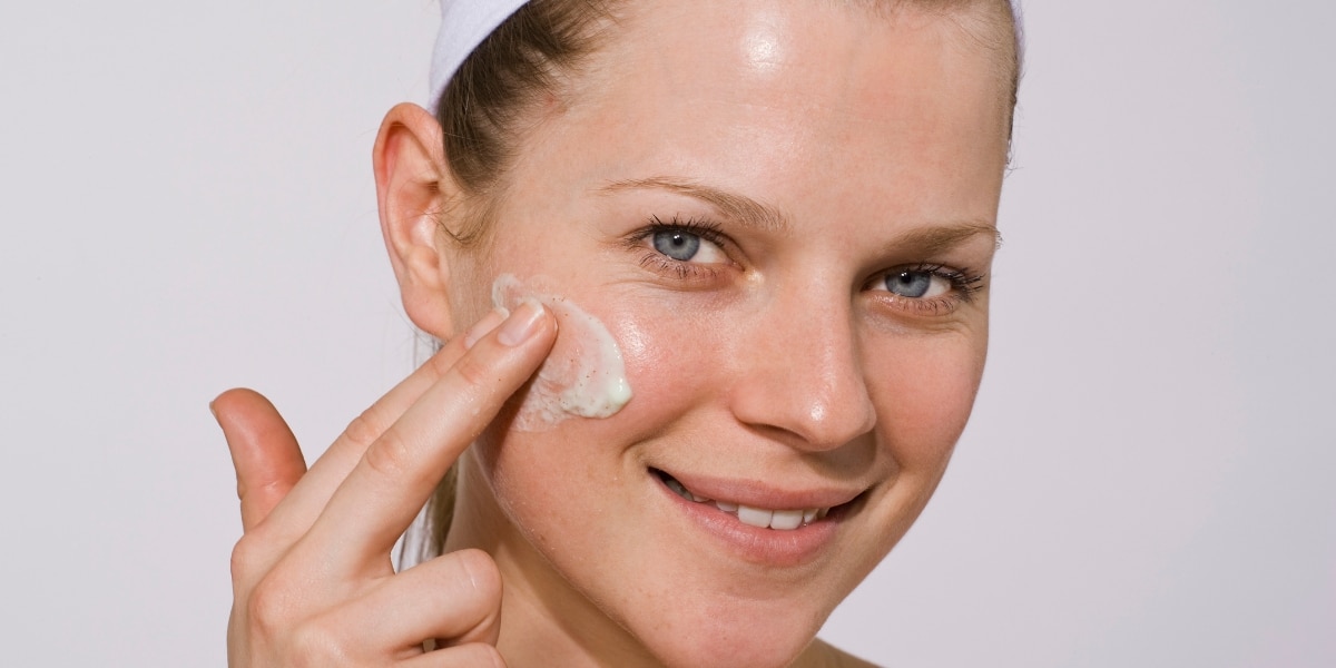 Smiling woman applying hydrating moisturizer to her face for soft and glowing skin.