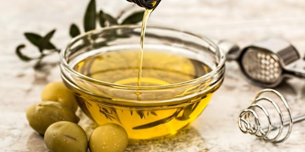 A bowl of olive oil being poured, showing its potential as a natural solution for healthier hair.