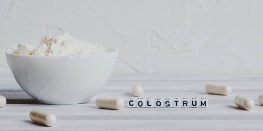 A bowl of colostrum powder with capsules on a table.