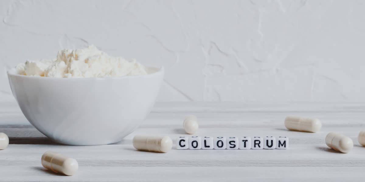 A bowl of colostrum powder with capsules on a table.